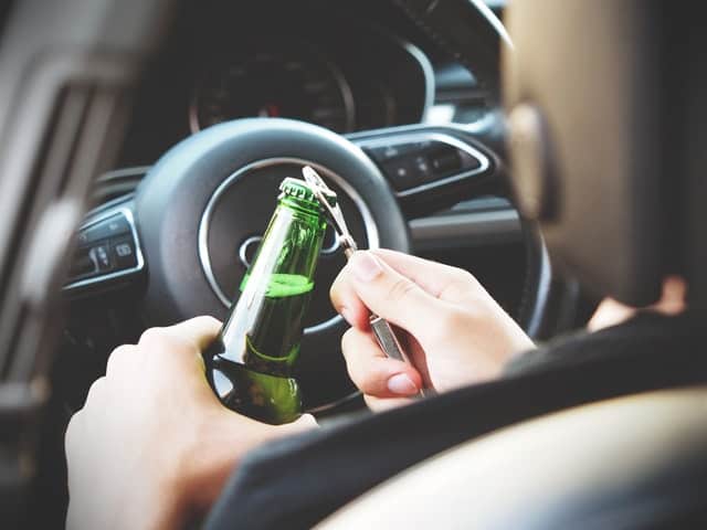 Image of a person opening a beer bottle in the driver's seat of a car