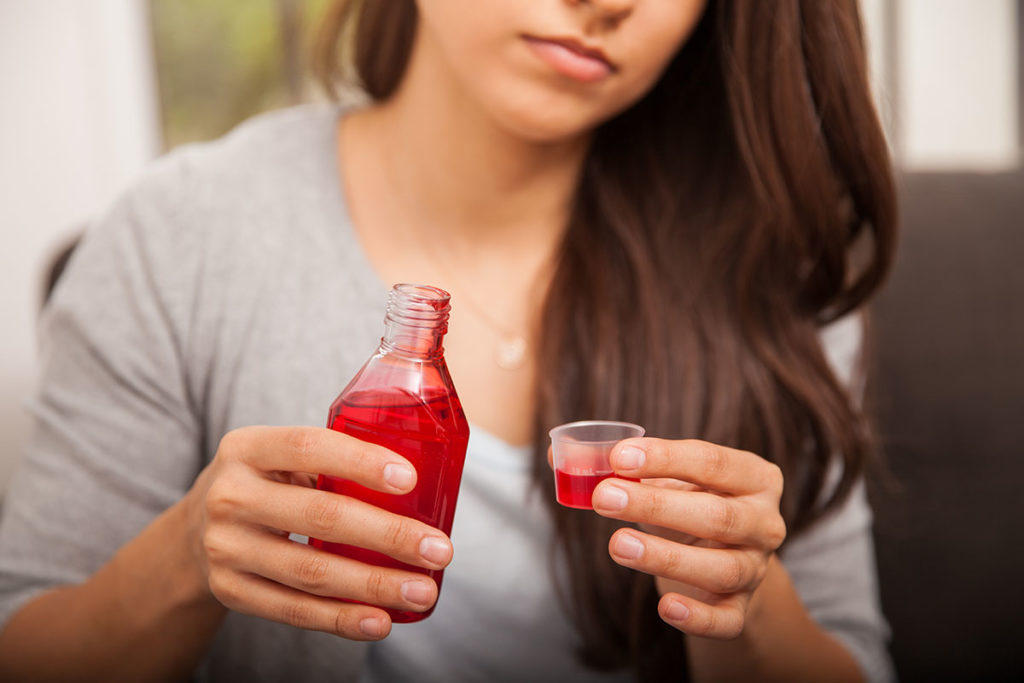 a person pours a dose of medicine wich could start the cycle of cough syrup abuse