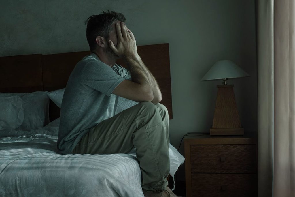 a person sits in a dark bedroom holding their face possibly struggling with Heroin Addiction