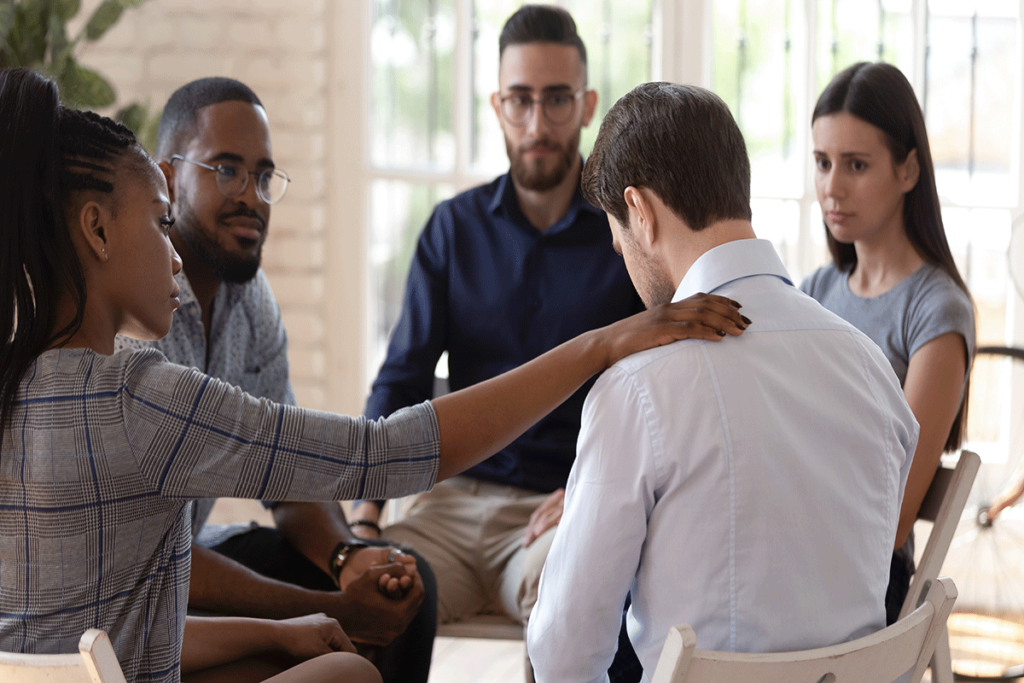 a person comforts another in a group after discussingmistakes during addiction treatment