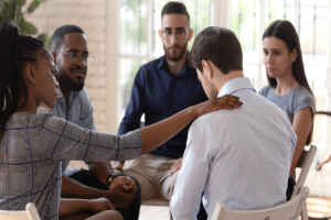a person comforts another in a group after discussingmistakes during addiction treatment