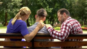 two parents sit on either side of a teen discussing teen marijuana use