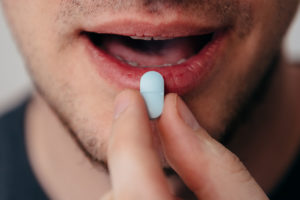 a hand guides a pill into a mouth it is important to recognize signs of vicodin addiction