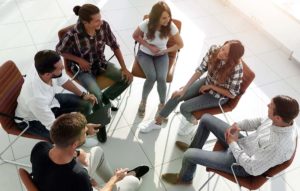 a group sits in a circle and talks one of the benefits of benefits of group therapy