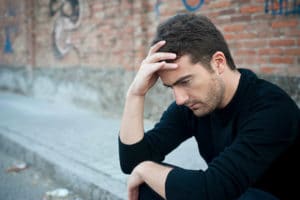 a person sits on a curb holding their head possibly struggling with signs of bipolar disorder