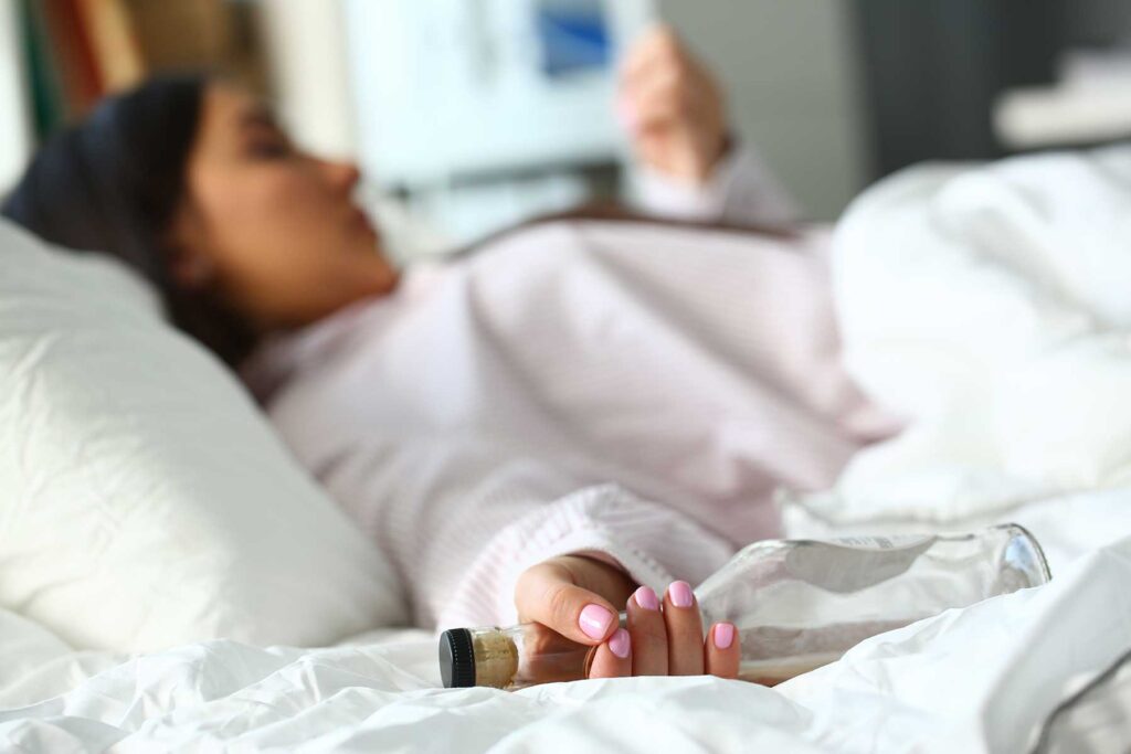 a woman lies in bed very sick from potential alcohol poisoning