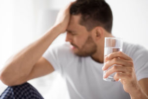 a person with signs of a heavy drinking problem has a headahce while holding a glass of water