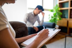 a person holds their head as a counselor takes notes during Therapy Treatment